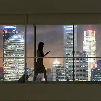 Silhouette of woman walking with luggage. Lit up cityscape in the background.