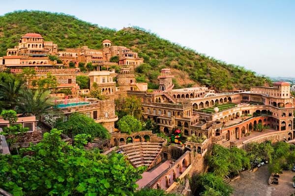 Exterior photo of the Neemrana Fort-Palace resort property. The photo depicts an imposing fort-like structure built into a lush hillside.