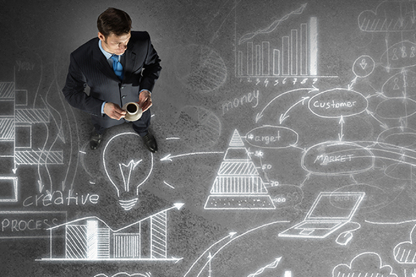 Business person superimposed onto chalkboard-like background with idea bubbles, graphs, charts, technologies, and flow charts, all meant to depict business strategizing.