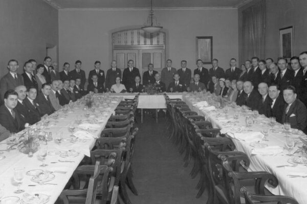 a group of people gathered around a u shaped dining room table.