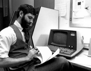 man sits at an early computer in the 1970s