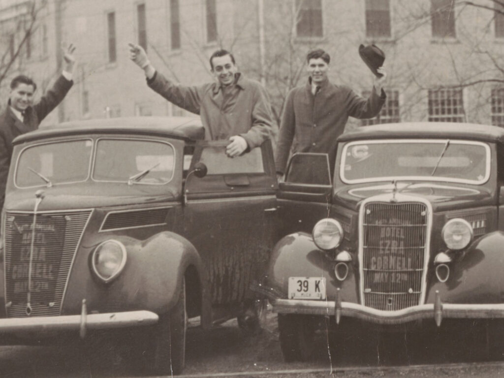 A group of men in front of cars.