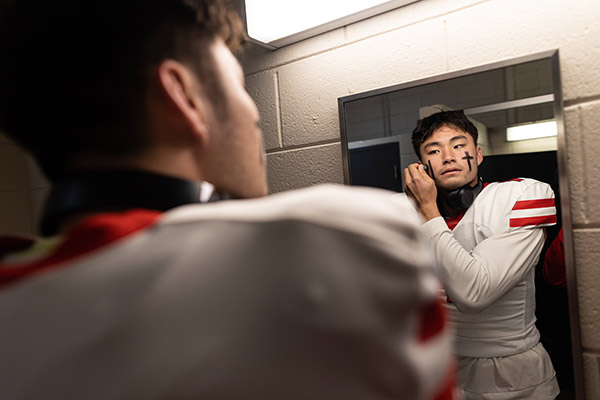 Jameson Wang looking in a mirror and applying eye black in a photo taken from behind and showing his reflection.
