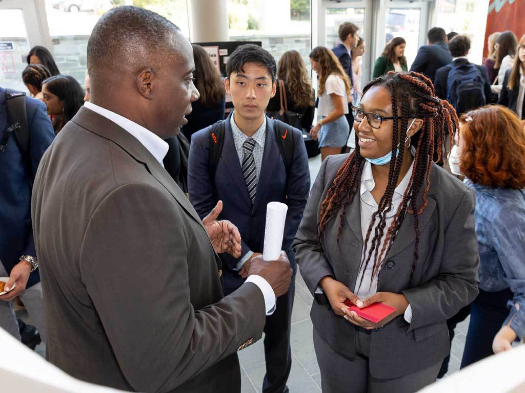 Alum in a suit speaks to two students in business attire.