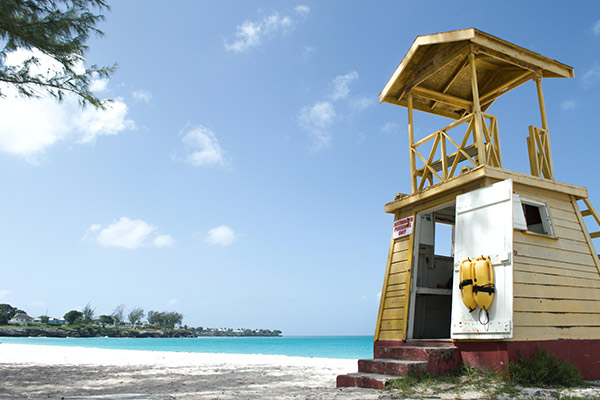 photo of a white sand beach and turquoise blue sea water with a wooden lifeguard station in the foreground.
