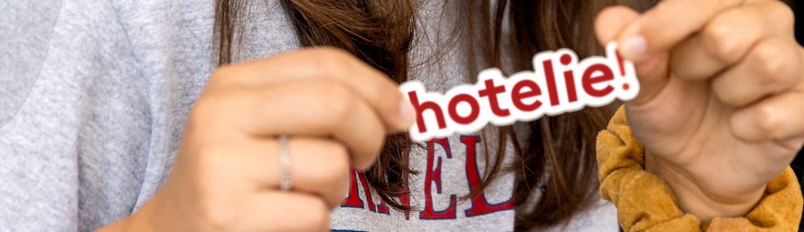 A person holds a sticker that says "hotelie!"