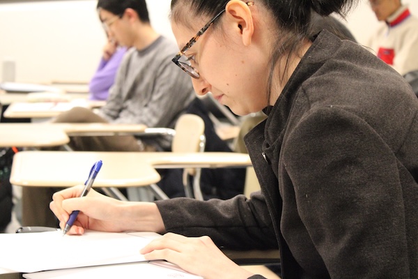 A student sits writing at a desk with a pen and paper.