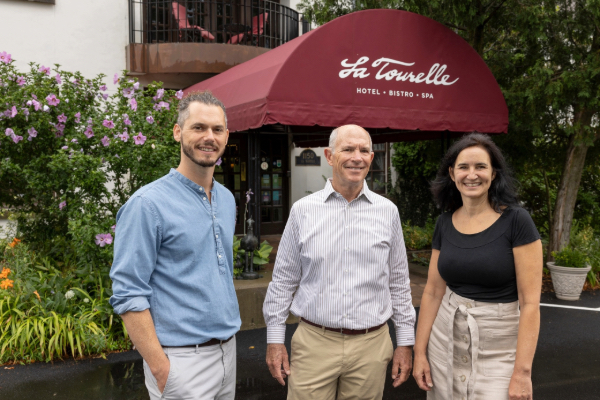 Bobby Frisch, Bill Minnock, and Lisa Chervinsky stand in front of the hotel entrance with the maroon La Tourelle awning behind them.