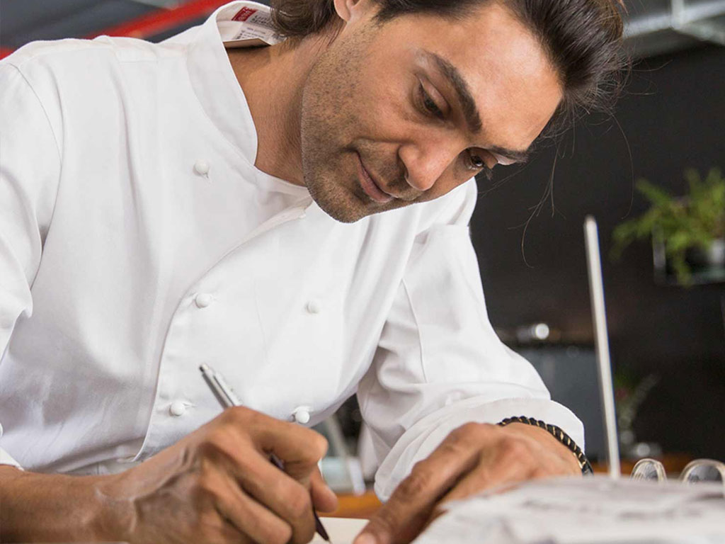 A man in white chef top writes with a pen.