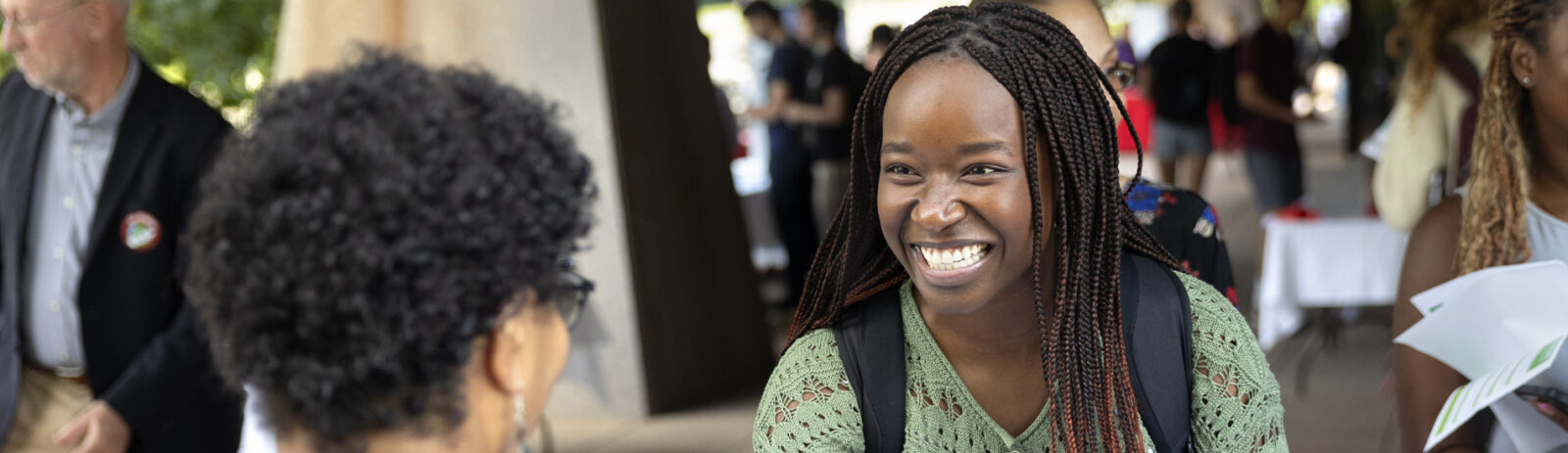 A student smiles with the back of another person’s head in the foreground.