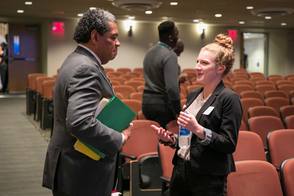 Two people in business attire talk in a tiered classroom.