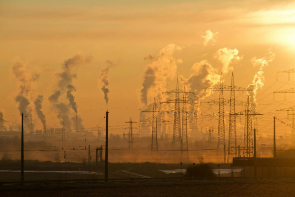 Smoke stacks and electrical wires are shown at a distance amid the yellow orange glow of the sunset.