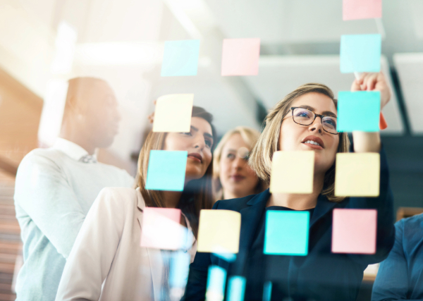 Colleagues look at post it notes on a glass board.