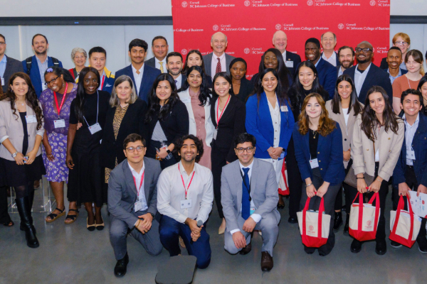 Group photo of speakers, organizers, and attendees on stage in front of a red Cornell banner.