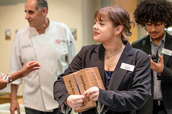 A person in business attire carrying a box with a chef and another manager behind them.
