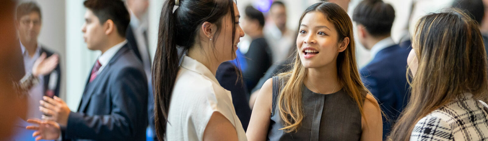 Two students in business attire talk to a representative at a club fair.