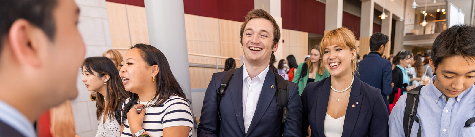 Two students in business attire talk to a representative at a club fair.