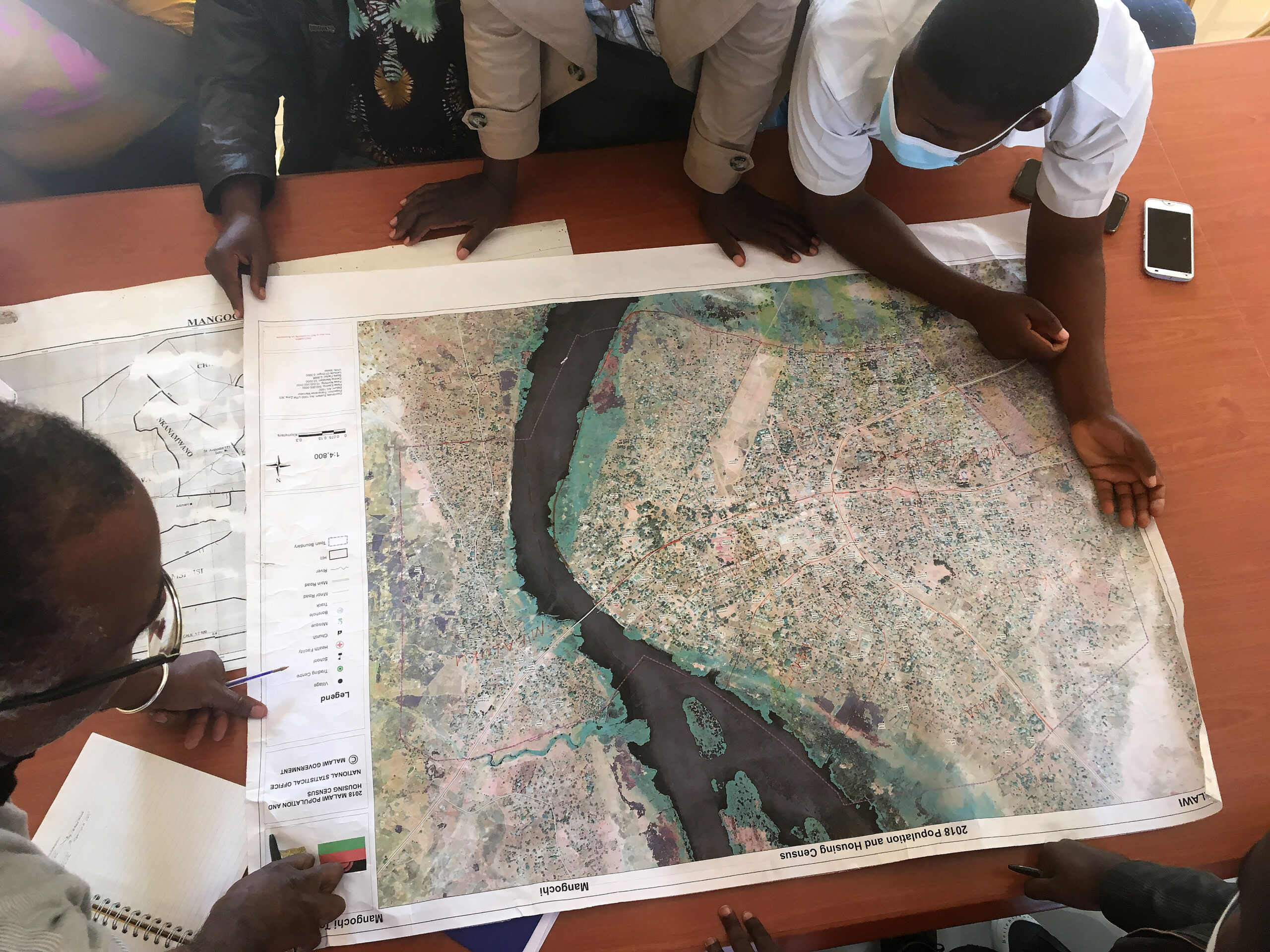 A group of people crowd around at a map with a river, the photo is taken from above.