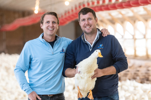 Two men, one holding a large white duck, smile.
