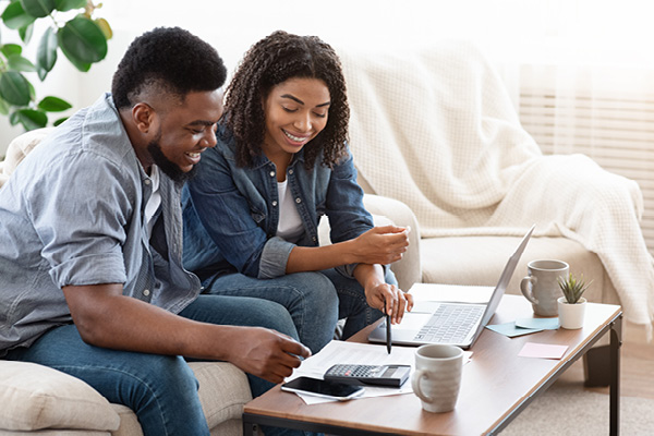 A young, happy couple budget together on their couch.