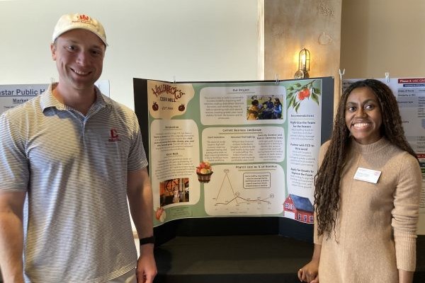Chelsey Turner and Evan Gold standing in front of their poster, showcasing their work for Hollenbeck’s Cider Mill.