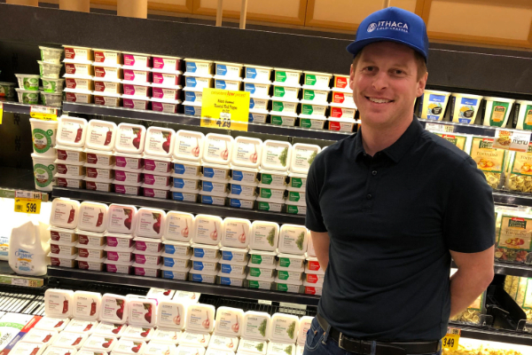 Chris Kirby '15 stands in front of a Ithaca Hummus display in a grocery store.
